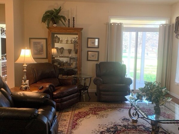 A living room with leather sofas, a coffee table, a lamp, a mirror, and a view through a glass door.