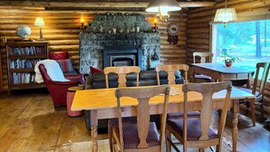 A rustic cabin interior with a fireplace, wooden furniture, and a bookshelf. - Blinn's Landing: Historic Riverfront Log Cabin, Dock & Mountain Views. Dogs OK! (Bend)