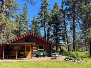 A log cabin with a porch, two green chairs, and a table.