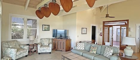 A spacious living room with a sofa, armchairs, a coffee table, and a television.