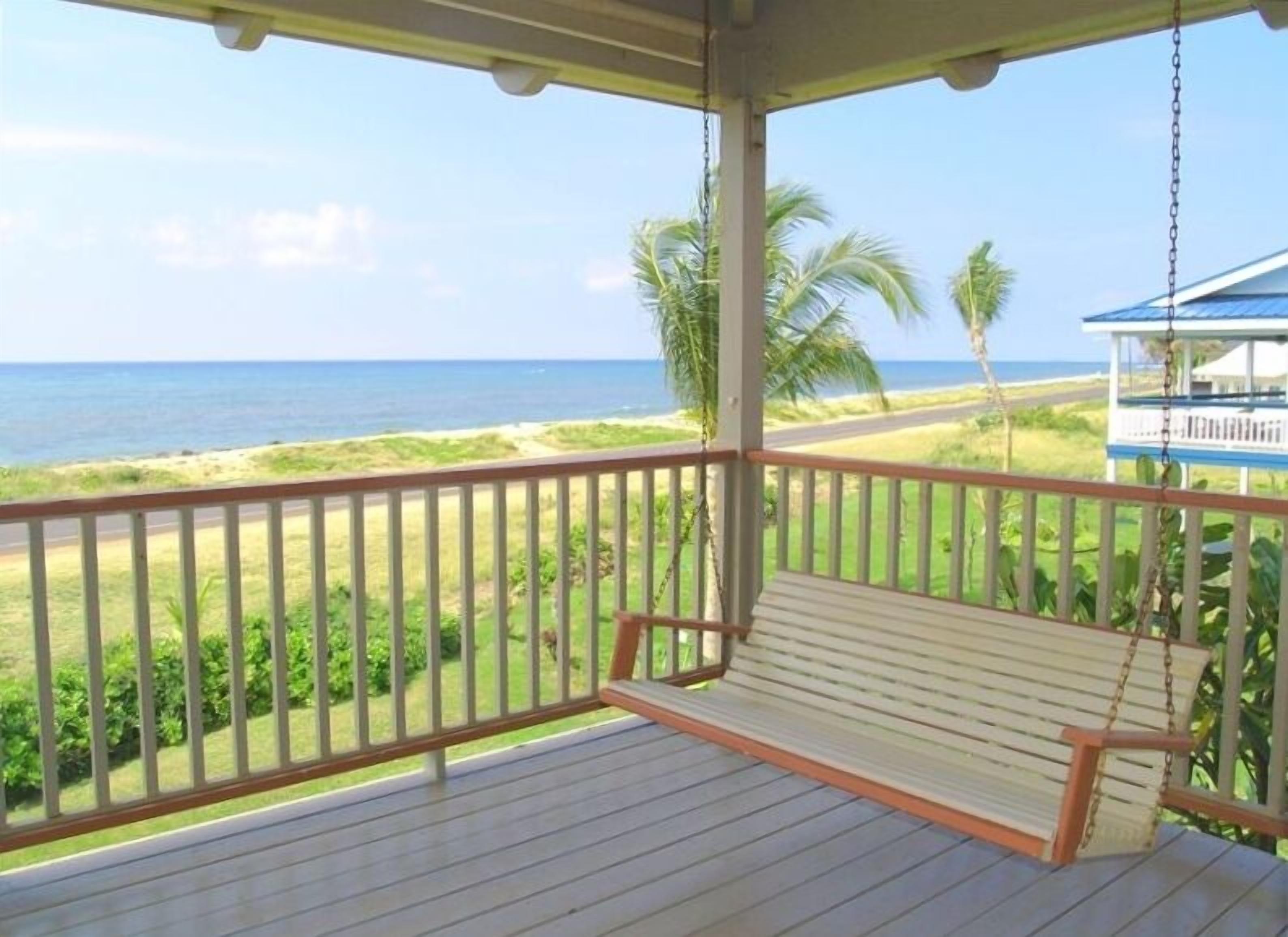 A wooden deck with a swing overlooking a beach and ocean.