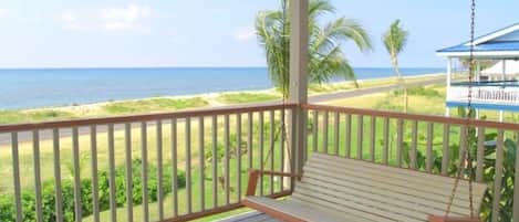 A wooden deck with a swing overlooking a beach and ocean.