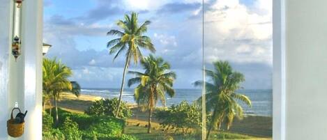 A bathroom with a large window offering a view of palm trees and the ocean.