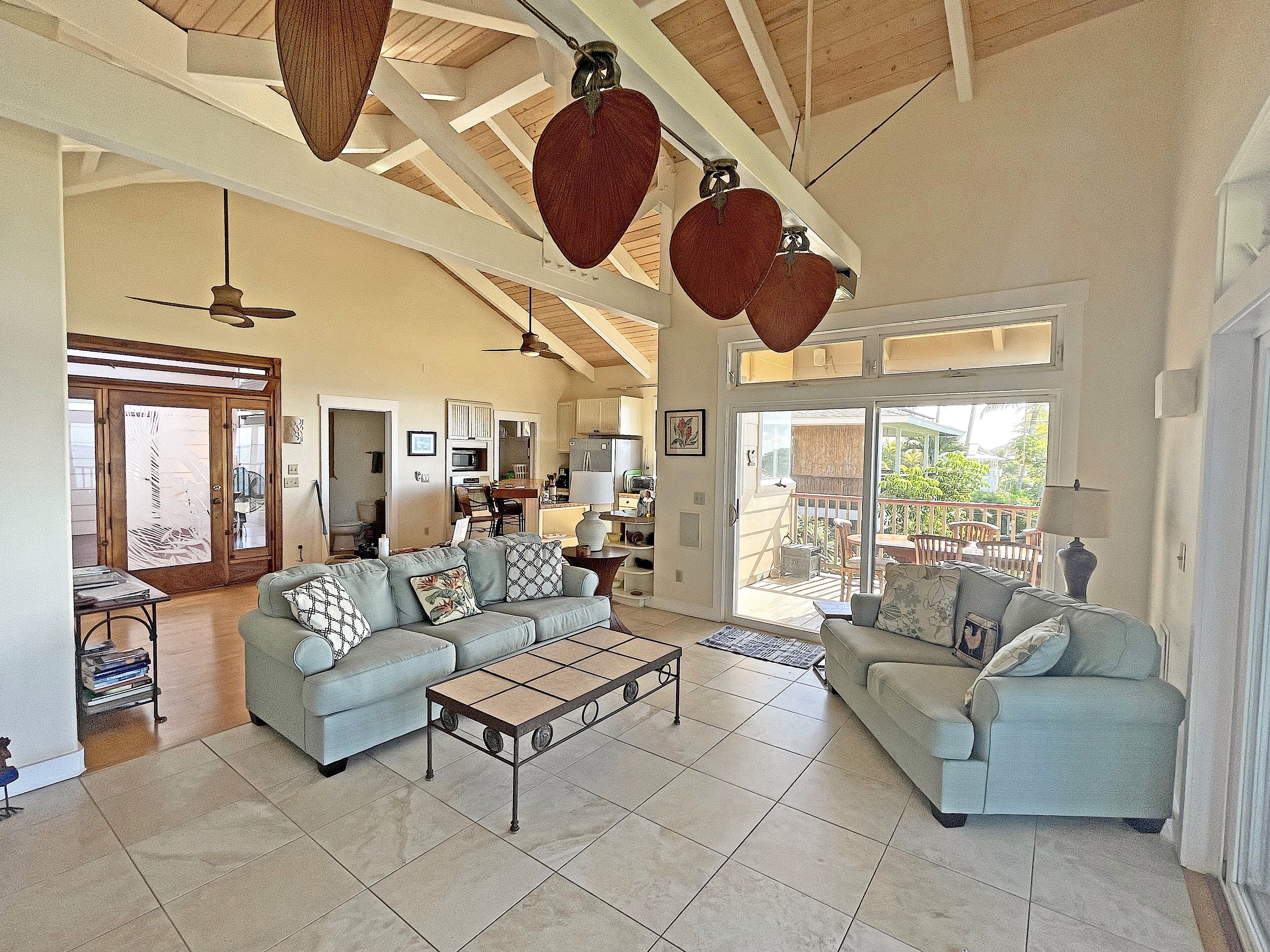 A spacious living room with two sofas, a coffee table, and a ceiling fan. There is a sliding glass door leading to a balcony.