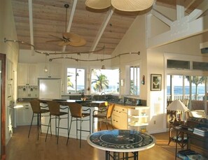 Enjoy ocean views from the large windows in this spacious room, featuring a central fan, kitchen island, and dining area with wicker chairs.
