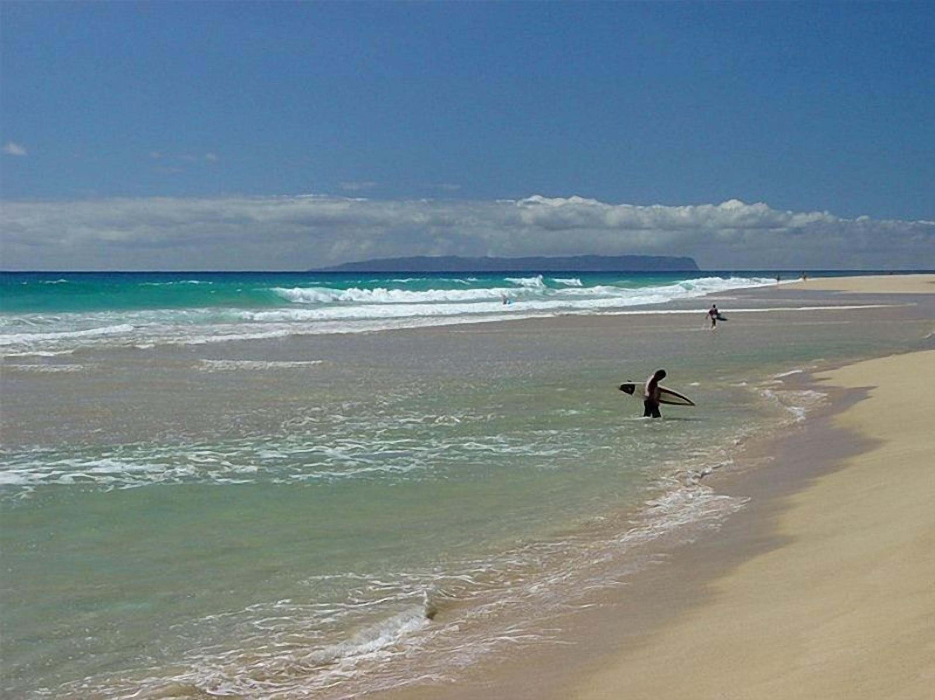 A beach with clear water, a sandy shore, and a distant mountain range.