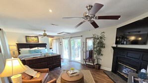 A spacious living room with a large bed, a fireplace, a ceiling fan, and a television. - River Front, Fishing, Kayaking, Boating, Tubing on the Edisto River   (Ridgeville)