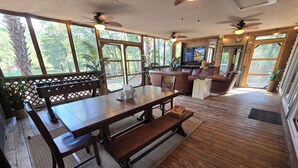 A wooden deck with a dining table, benches, and a TV. - River Front, Fishing, Kayaking, Boating, Tubing on the Edisto River   (Ridgeville)