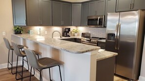 A modern kitchen with grey cabinets, stainless steel appliances, a marble countertop, and bar stools. - Lakefront 311 - Updated Lake Front villa just steps to the beach and pools! (Miramar Beach)