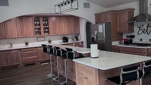 Una cocina moderna con armarios de madera, una isla grande con taburetes de bar, un ventilador de techo y un letrero que dice 'Eat'.