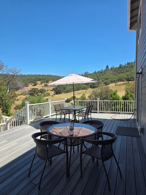A deck with a table and chairs, a patio umbrella, and a view of a hilly landscape.
