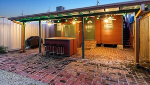 A covered patio with a brick floor, a bar area with stools, and a staircase leading to an upper level. - The Tchoup House, Rock out Nextdoor to Tipitina’s music club Uptown (new orleans)