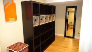 A hallway with a dark wooden bookshelf, a wicker basket, and a mirror reflecting a room with a chair.