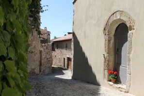 A narrow cobblestone street with stone buildings, one with a door and a potted plant. - Spacious, light and beautifully renovated. A home from home for the discerning. (Caunes-Minervois)