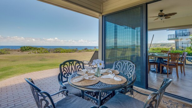An outdoor dining area with a table set for two, overlooking a scenic view of the ocean. - Kapalua Bay Villa 35G4 | Sunset Views | Walk to Beach (Lahaina)