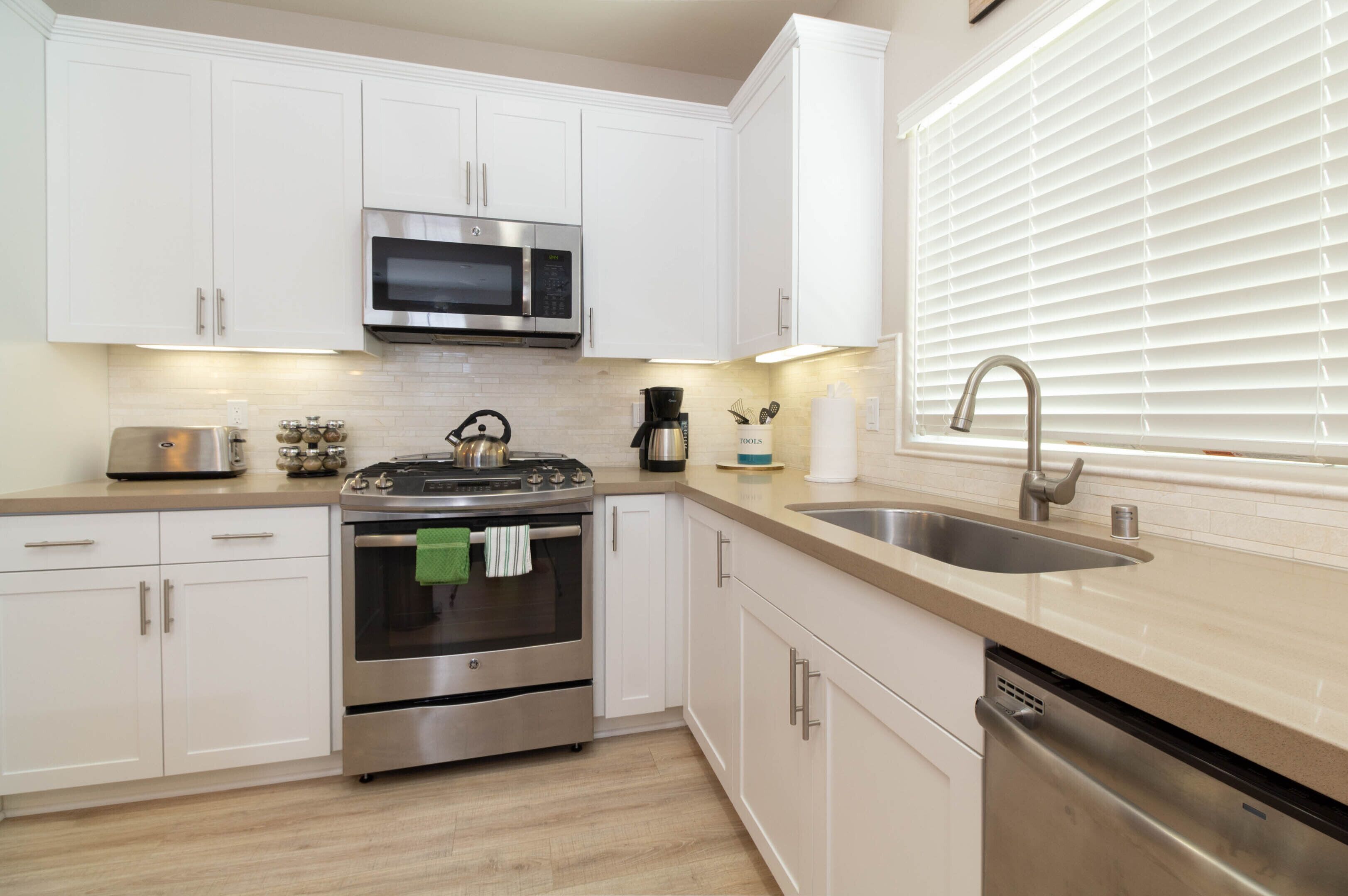 A modern kitchen with white cabinets, stainless steel appliances, a built-in oven, and a sink.