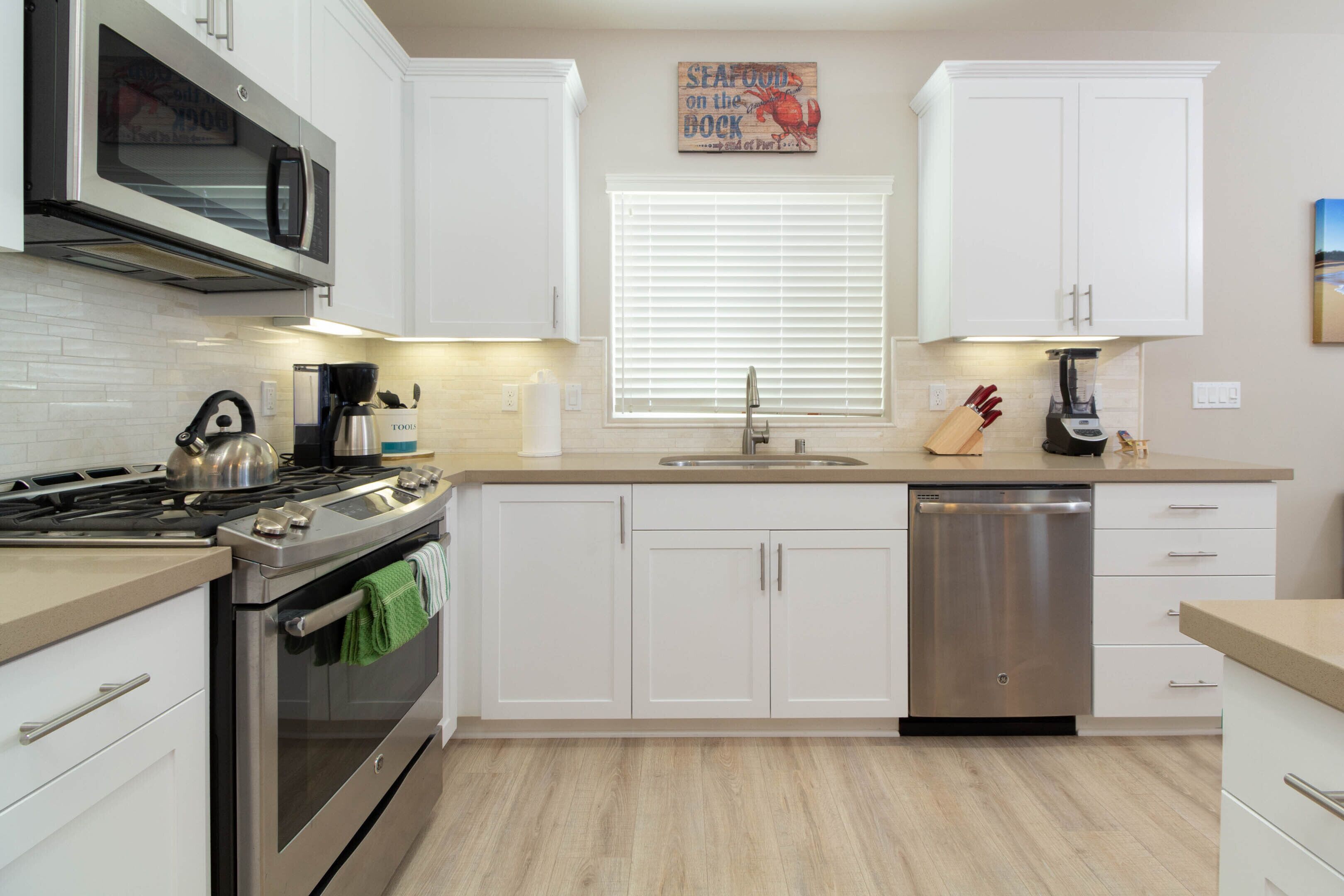 A modern kitchen with white cabinets, stainless steel appliances, and a wooden floor.
