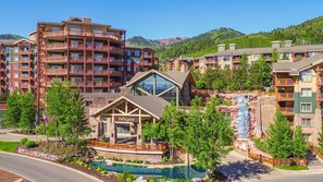 Ein mehrstöckiges Hotel mit Balkonen, einem Poolbereich und Blick auf eine Berglandschaft.