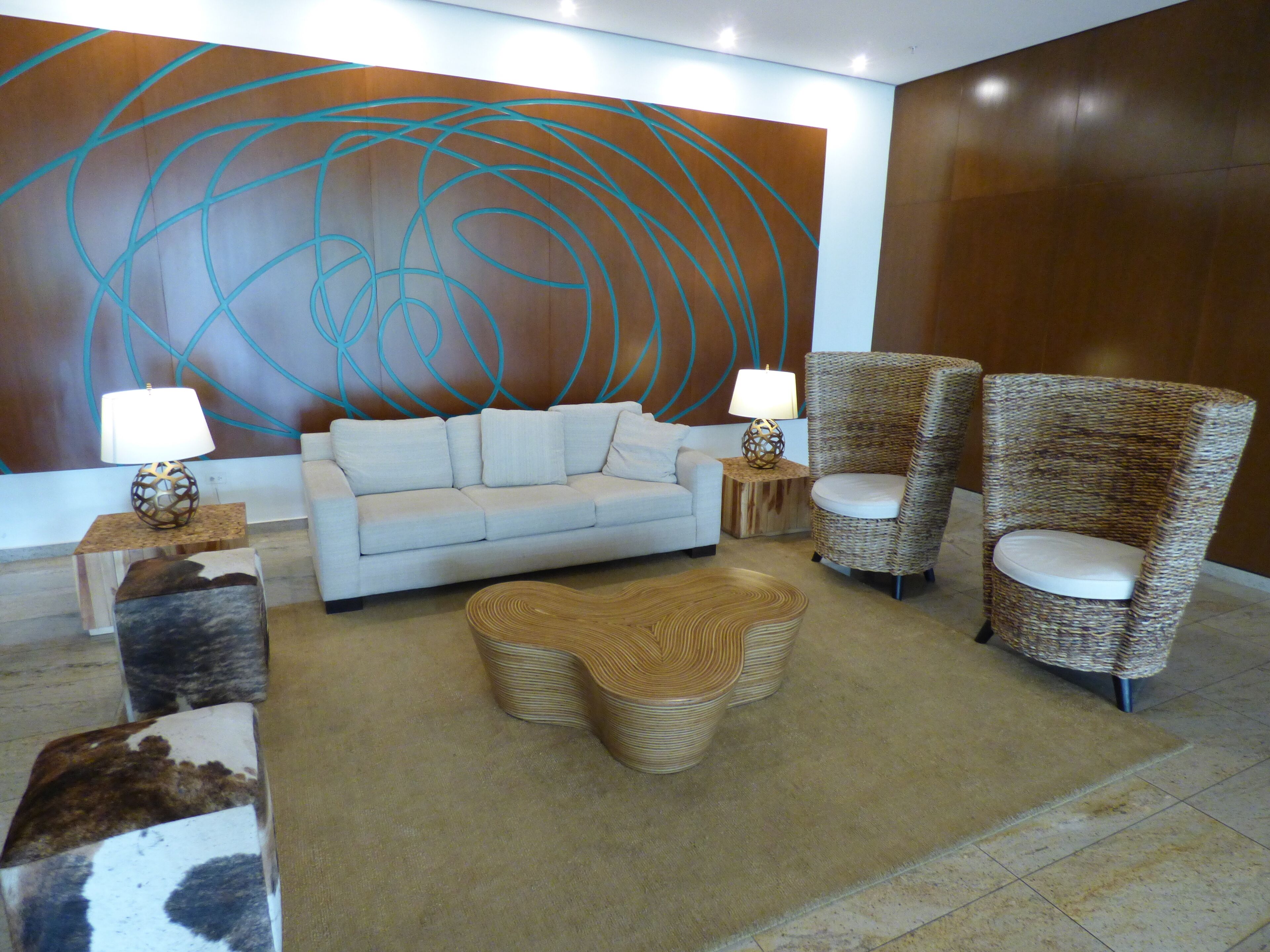 Un salon moderne comprenant un canapé, deux fauteuils, une table basse et un mur décoratif orné d’œuvres d’art abstraites.