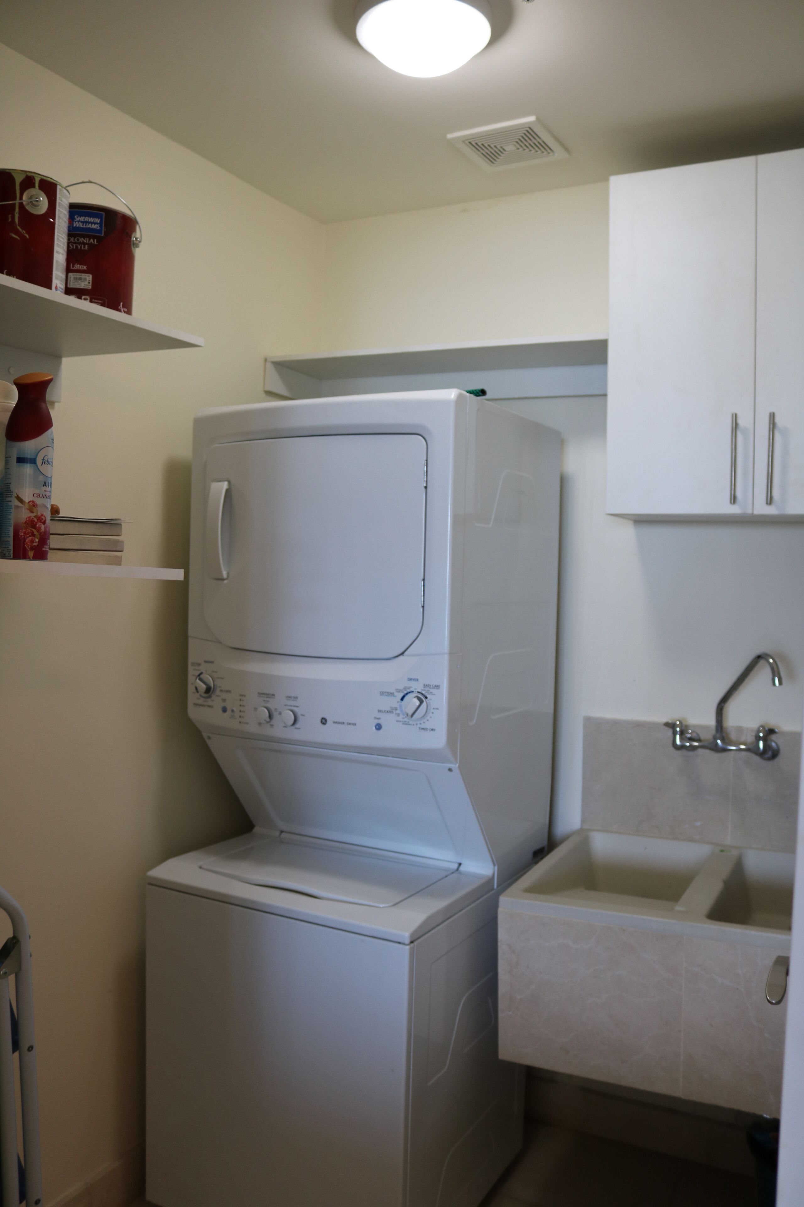 A compact laundry area with a front-loading washer and dryer, a small sink, and storage shelves.
