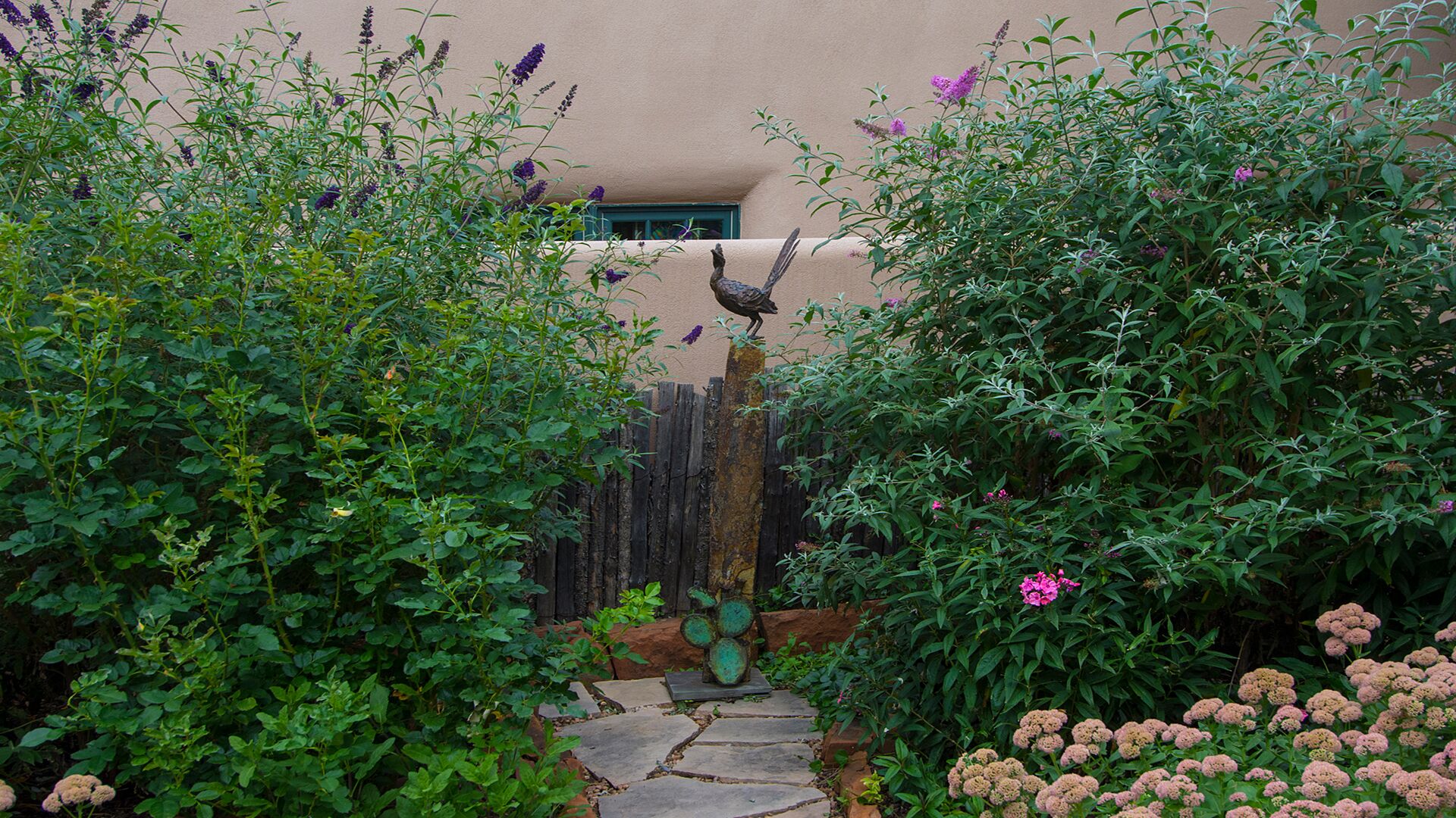 A garden pathway leading to a building with a wooden fence and a bird sculpture.