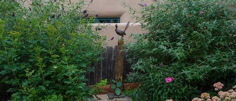 A garden pathway leading to a building with a wooden fence and a bird sculpture.