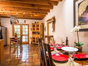 Comedor con mesa de madera dispuesta para cuatro, platos rojos y copas de vino.