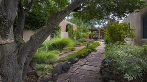 Un sendero de piedra que atraviesa un jardín con diversas plantas y una estructura de pérgola.