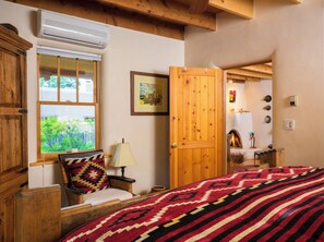 A cozy room with a bed, a window, an air conditioner, a lamp, a door, and a fireplace. - READ OUR REVIEWS!! Enchanting art-filled adobe, lush gardens, easy walk to Plaza (Santa Fe)
