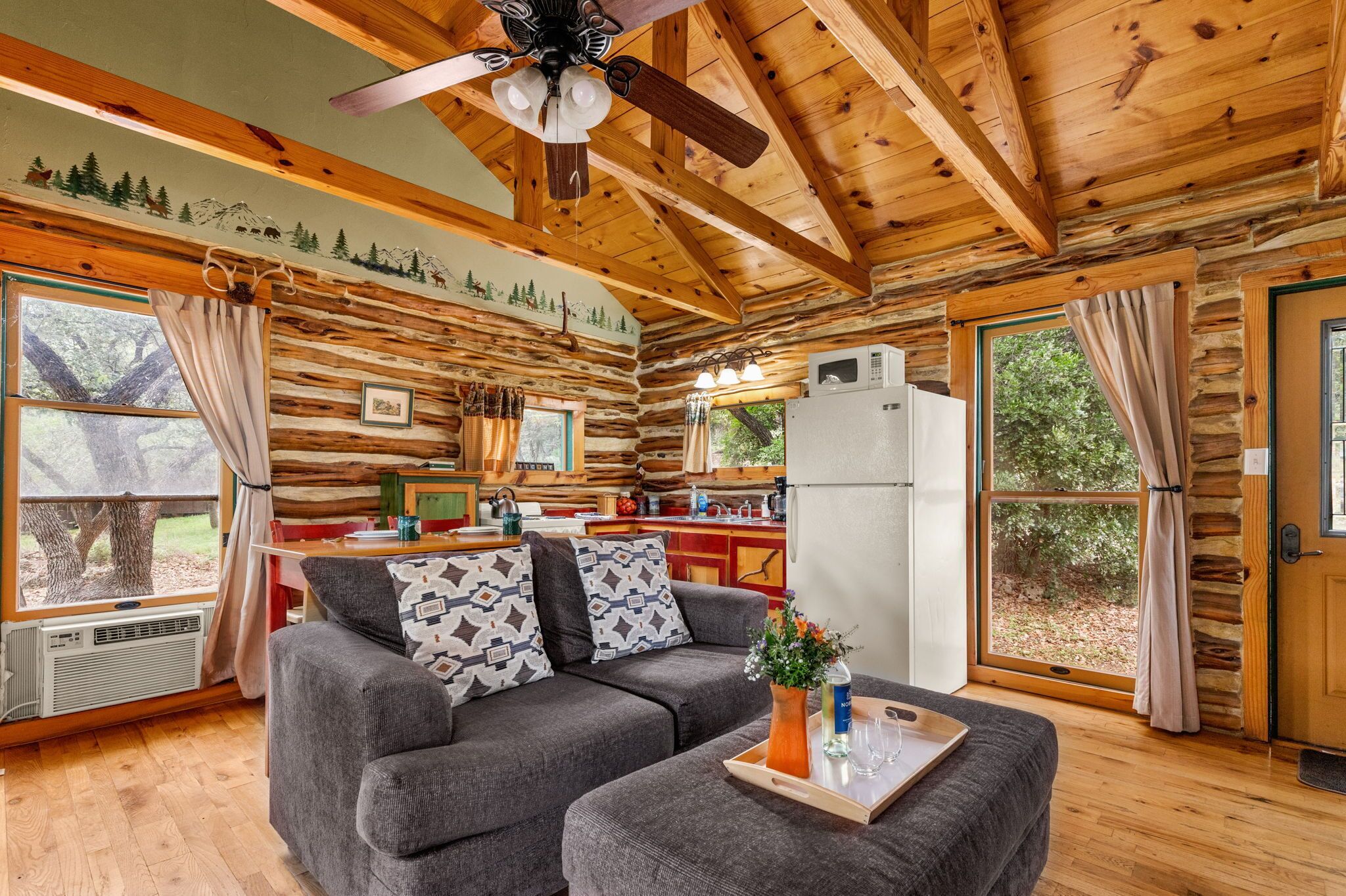 Ein rustikales Blockhaus-Interieur mit Holzbalkendecke, einer Couch, einem Esstisch und einer Küchenzeile.
