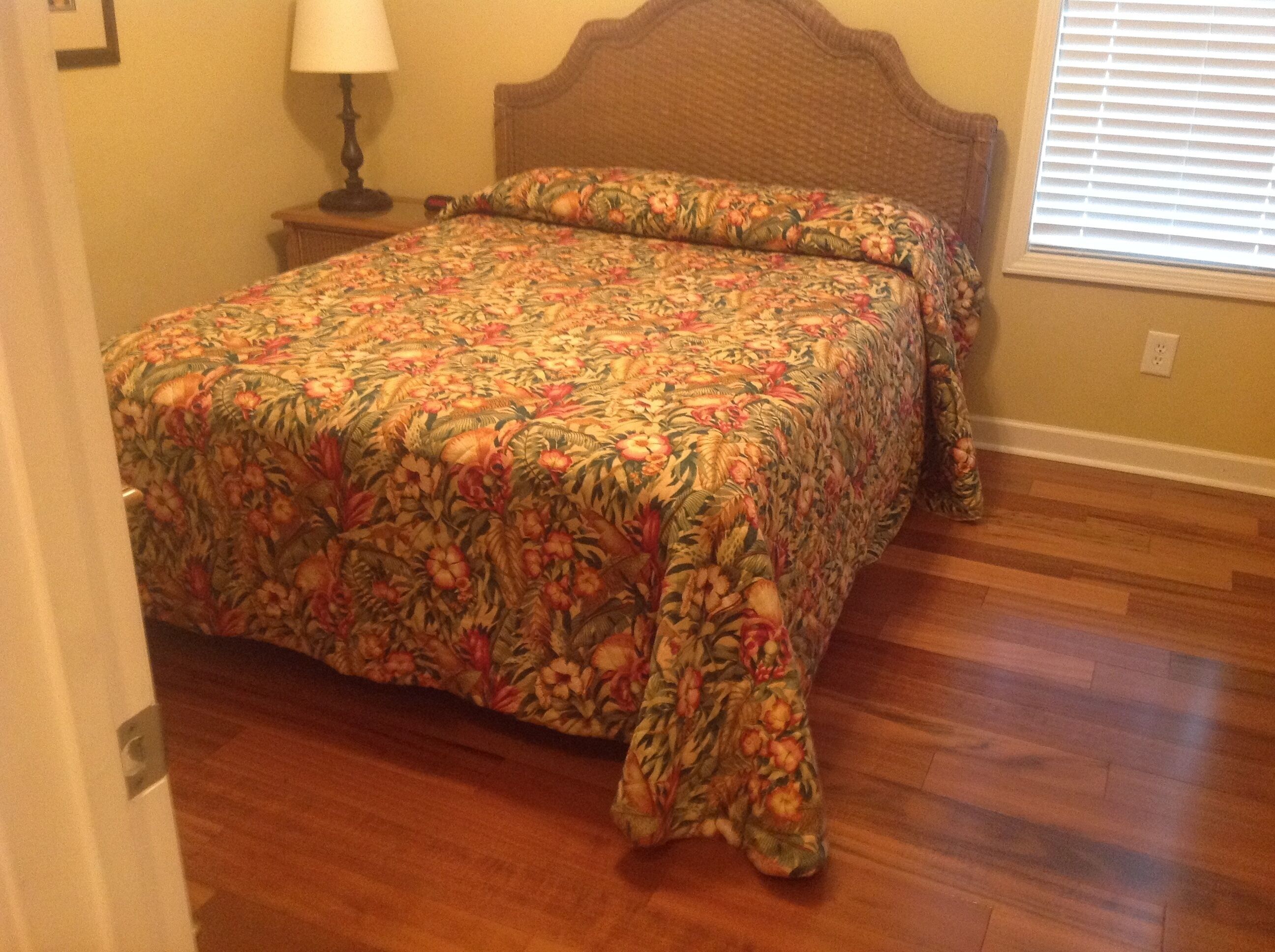 A bedroom with a floral bedspread, wooden headboard, and a nightstand with a lamp.