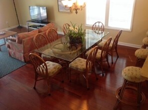 Un coin repas avec une table à plateau en verre, entourée de chaises en osier agrémentées de coussins à motifs floraux.