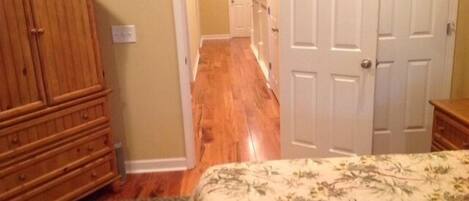 A bedroom with a wooden wardrobe, a floral bedspread, and a carpeted floor.