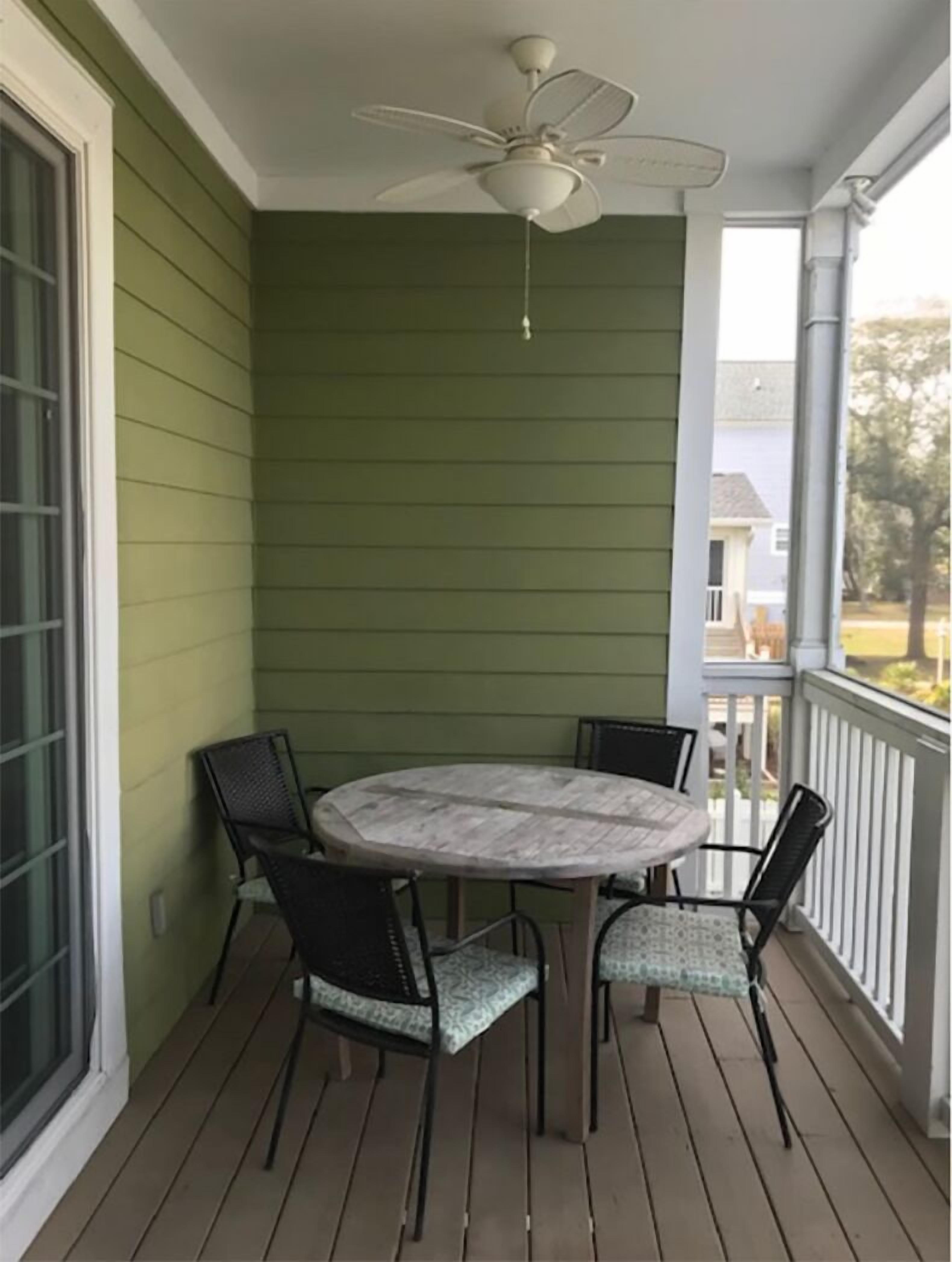 A covered porch with a round table and four chairs, a ceiling fan, and a view of a residential area.