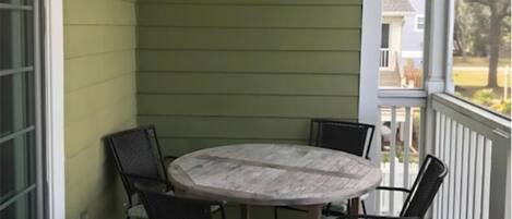 A covered porch with a round table and four chairs, a ceiling fan, and a view of a residential area.