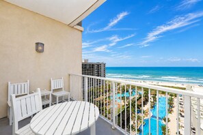 Ein Balkon mit weißer Möbel, Blick aufs Meer und ein Poolbereich.