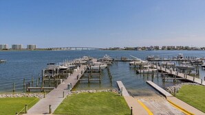 A marina with docks and boats, a grassy area, and a bridge in the background. - Phoenix on the Bay 1233 | Orange Beach, AL (Orange Beach)