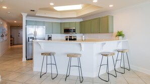 A modern kitchen with a central island, green cabinets, and a stainless steel refrigerator. - Phoenix on the Bay 1233 | Orange Beach, AL (Orange Beach)