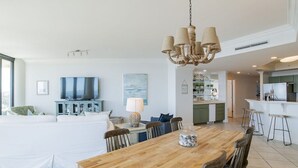 A spacious living room with a large wooden dining table, a chandelier, and a TV. - Phoenix on the Bay 1233 | Orange Beach, AL (Orange Beach)