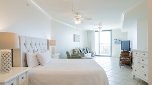 A hotel room with a large bed, a ceiling fan, a TV, and a balcony with a view. - Phoenix on the Bay 1233 | Orange Beach, AL (Orange Beach)