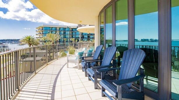 A balcony with chairs, a railing, and a view of a building and water. - Phoenix on the Bay 1233 | Orange Beach, AL (Orange Beach)