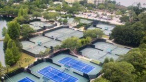 Eine Vogelperspektive eines Sportkomplexes mit mehreren Tennisplätzen, umgeben von Grünflächen und Gebäuden.