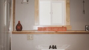 Ein Badezimmer mit einem Holzregal, einer Vase, einem Schild und einem Waschbecken.