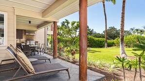 Un patio techado al aire libre con sillones, una mesa y zona de barbacoa.