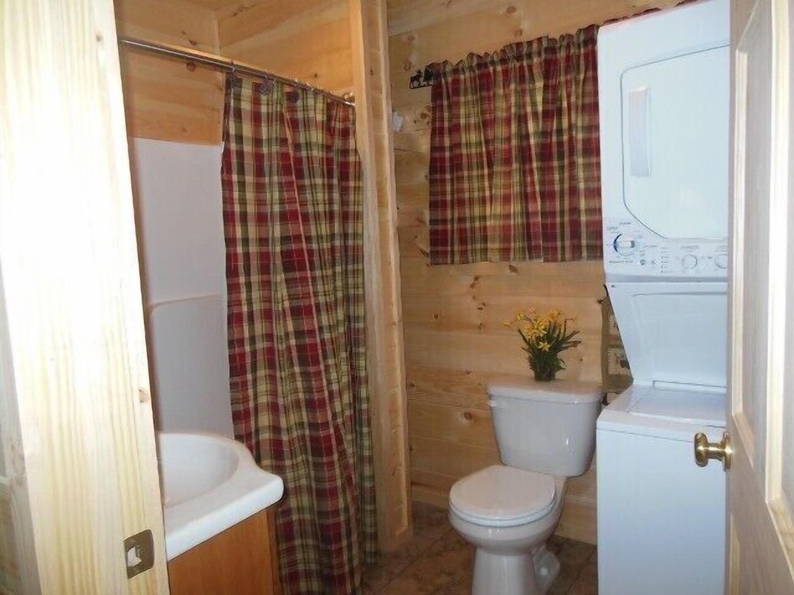 A small, wooden bathroom with a toilet, a sink, and a shower area.