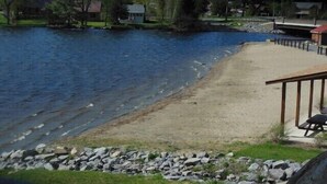 A riverside view with a sandy beach, a wooden deck, and a stone barrier. - ENJOY SUMMER IN THE ADIRONDACKS AT RUBY HILL CABINS (Wells)