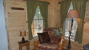 A cozy cabin interior with a wooden chair, a lamp, and a window with curtains. - ENJOY SUMMER IN THE ADIRONDACKS AT RUBY HILL CABINS (Wells)