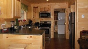 A wooden cabin kitchen with a central island, a microwave, stove, refrigerator, and a sink. - ENJOY SUMMER IN THE ADIRONDACKS AT RUBY HILL CABINS (Wells)