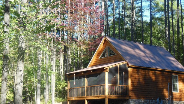 A cabin with a porch, surrounded by trees and rocks. - ENJOY SUMMER IN THE ADIRONDACKS AT RUBY HILL CABINS (Wells)