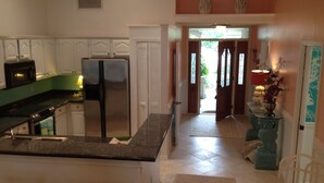 A kitchen with white cabinets, a stainless steel refrigerator, and a granite countertop. There is a wooden stool and a chair in the foreground.